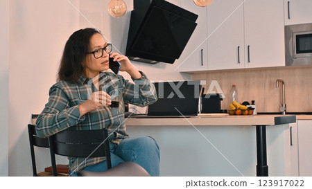 Woman Taking a Work Call While Relaxing in a Modern Kitchen Woman Taking a Work Call While Relaxing in a Modern Kitchen 123917022