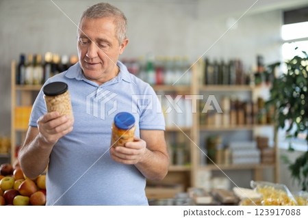 Senior man is holding two glass jars of preserves in hands, choosing pickled beans 123917088