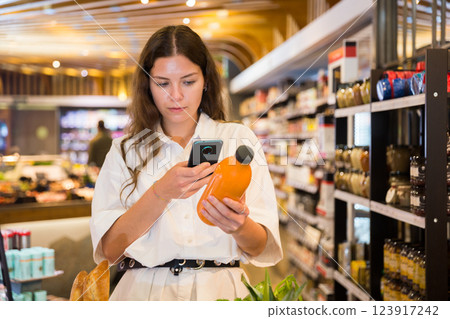 Focused girl chooses carrot juice in a supermarket, studying its composition on the bottle Focused girl chooses carrot juice in a supermarket, studying its composition on the bottle 123917242