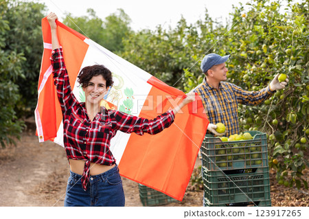 Joyful young Latin female gardener waving Peruvian flag during lemon harvesting season on farm in autumn Joyful young Latin female gardener waving Peruvian flag during lemon harvesting season on farm in autumn 123917265