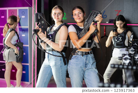 Two cheerful and happy girls friends pose in locker room before laser tag match. Two cheerful and happy girls friends pose in locker room before laser tag match. 123917363