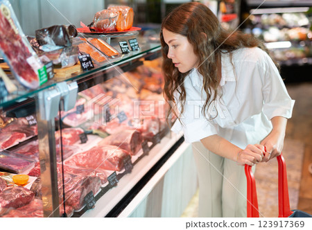 Young girl examines the production in the department of the butcher shop in the supermarket 123917369