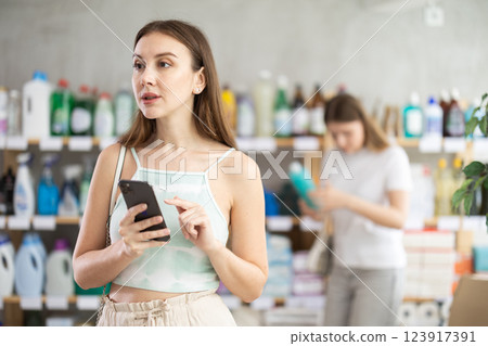 Young woman with phone chooses household chemicals in store Young woman with phone chooses household chemicals in store 123917391