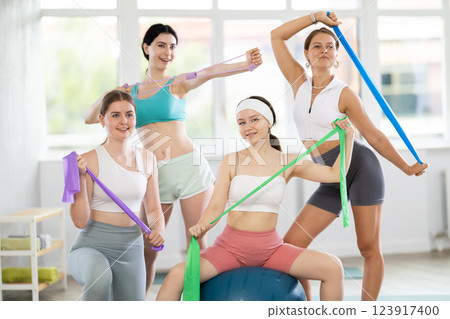 Portrait of sporty girls in sportswear with fitness balls and resistance bands posing together in sports studio, ready for training Portrait of sporty girls in sportswear with fitness balls and resistance bands posing together in sports studio, ready for training 123917400