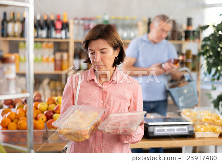 Woman chooses chicken or pork fillet, while her husband buys alcohol in supermarket Woman chooses chicken or pork fillet, while her husband buys alcohol in supermarket 123917480