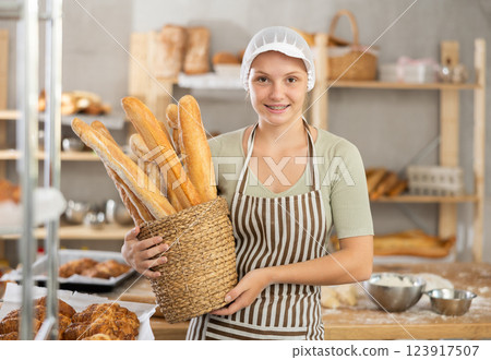 Young female baker with basket of baguettes Young female baker with basket of baguettes 123917507