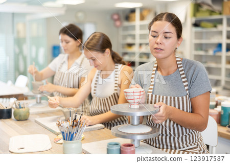 Three craftsperson are busy sculpting from clay and painting ceramic products Three craftsperson are busy sculpting from clay and painting ceramic products 123917587