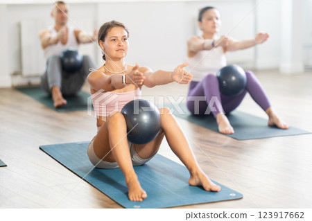 Young female Pilates instructor performing sit-ups with ball with group 123917662