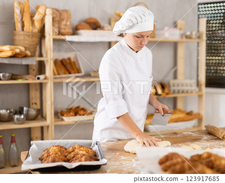 Female baker preparing dough, kneading it on kitchen table 123917685