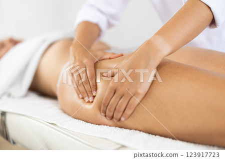 Experienced masseuse performing manual massage on anterior thighs to woman Experienced masseuse performing manual massage on anterior thighs to woman 123917723