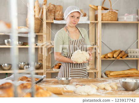 Adolescence girl works in bakery as baker, kneads dough, works with flour. 123917742