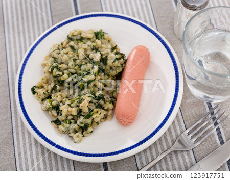 Boiled unpeeled sausage with side dish of pearl barley with spinach. Boiled unpeeled sausage with side dish of pearl barley with spinach. 123917751