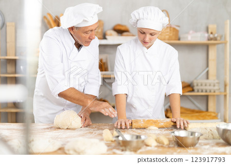 Pensioner man and girl make dough, employee kneads lump of dough, assistant works with rolling pin 123917793