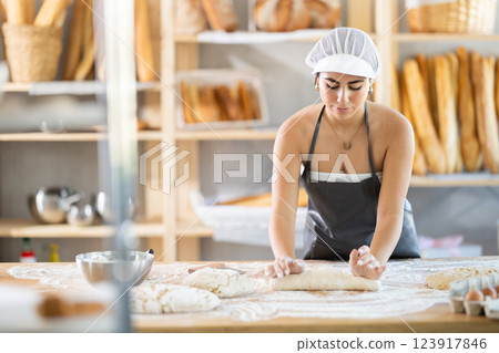 Young female baker kneading dough on table Young female baker kneading dough on table 123917846