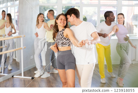 Happy young man and girl with group of international dancers training active swing in dance class Happy young man and girl with group of international dancers training active swing in dance class 123918055