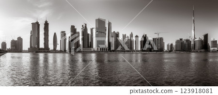 Monochrome city skyline with tall skyscrapers reflecting on calm water under a cloudy sky, Dubai Marina bay UAE 123918081