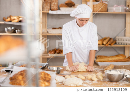 Young female baker kneading dough in small bakery Young female baker kneading dough in small bakery 123918109