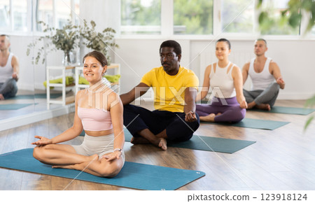 Smiling girl meditating in lotus position during group yoga session Smiling girl meditating in lotus position during group yoga session 123918124