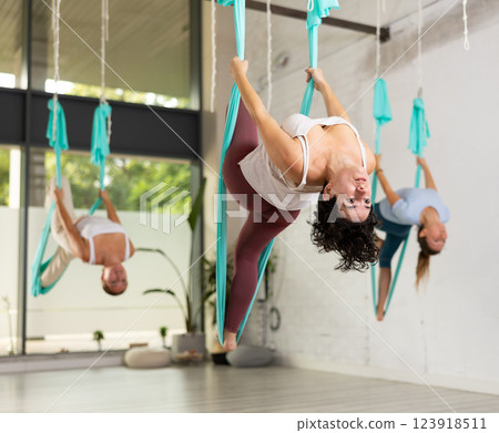 Young Latin woman practicing aerial yoga asana, hanging head down in fitness club. Health, sport, yoga concept 123918511