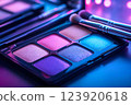 A close-up of a colorful makeup palette with shimmering eyeshadows and makeup brushes under neon lights 123920618