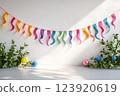 Colorful twisted paper garland hanging against a white wall with green plants and small decorative balls on the floor 123920619