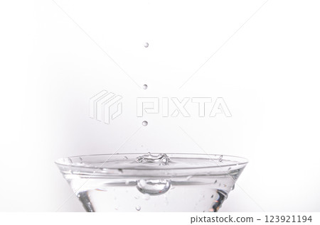 Close-up of water drop falling into a glass on white background Close-up of water drop falling into a glass on white background 123921194
