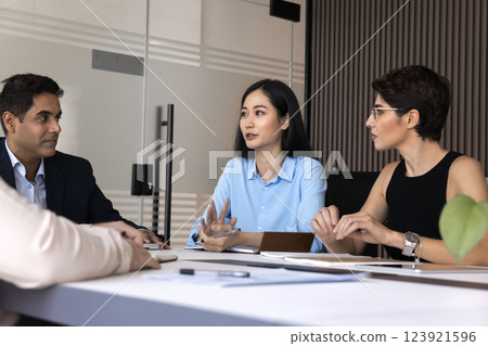 Diverse business partners listen to young Asian woman at table 123921596