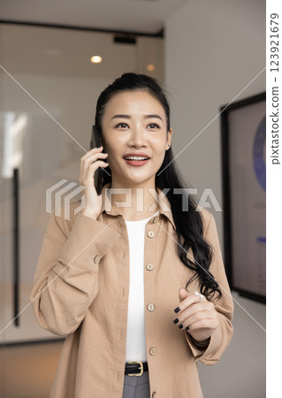 Thoughtful positive young Asian businesswoman talking on mobile phone 123921679