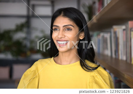 Headshot portrait pretty young girl standing by bookshelf with smile 123921826