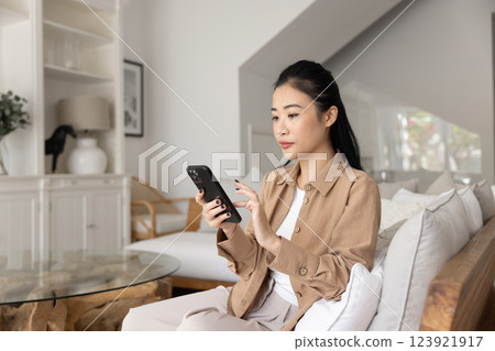 Focused beautiful young adult Asian girl using smart home application 123921917