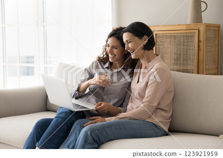 Aged mom grownup daughter spend time on couch using notebook 123921959