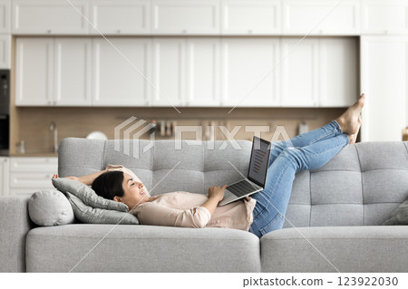 Happy young female freelancer work lying on sofa using notebook Happy young female freelancer work lying on sofa using notebook 123922030