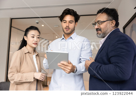Confident young project manager showing content on tablet to colleagues Confident young project manager showing content on tablet to colleagues 123922044