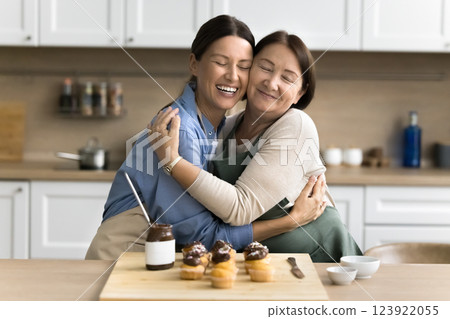 Young daughter cuddling tightly her older smiling mother in kitchen 123922055