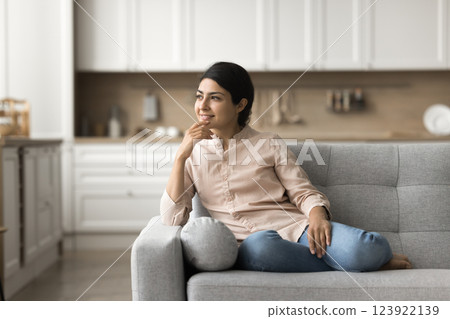 Mindful young lady sitting on couch smiling looking at distance 123922139