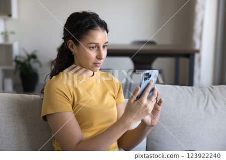 Teen girl using smartphone seated on sofa in living room 123922240