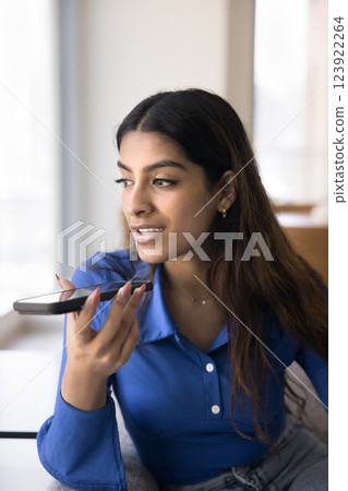 Focused Indian woman holding smartphone near her mouth 123922264