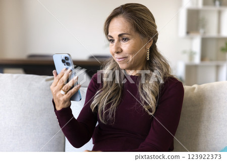 Woman sits on sofa videocalling using application on smartphone Woman sits on sofa videocalling using application on smartphone 123922373