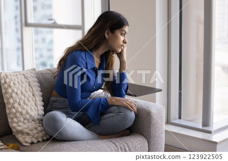 Woman sitting by window looking outside with pensive expression 123922505