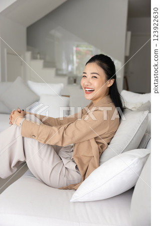 Happy cheerful young Vietnamese homeowner woman resting on comfortable sofa Happy cheerful young Vietnamese homeowner woman resting on comfortable sofa 123922630