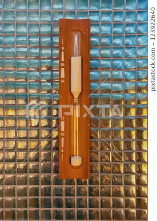 Wooden sand timer for sauna mounted on a glass mosaic wall. Traditional timekeeping device for steam bath sessions 123922640