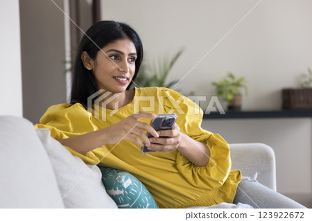 Woman chatting on smartphone seated on sofa in living room 123922672