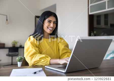 Happy Indian woman working remotely sit at table with laptop 123922681