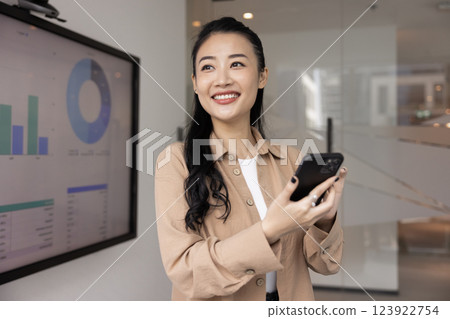 Positive beautiful young Asian project manager girl holding smartphone 123922754