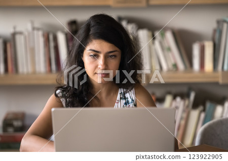 Thoughtful girl student busy with learning on notebook in library Thoughtful girl student busy with learning on notebook in library 123922905