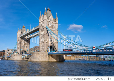 On a bright sunny day in London, Tower Bridge stands majestically over the River Thames. The iconic structure captures the essence of British architecture while a red bus crosses above. 123922917