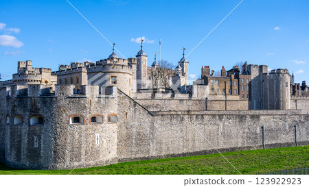 Tower of London stands proudly along the River Thames, showcasing its medieval structure and rich history. Visitors admire its impressive walls and iconic towers under a clear blue sky. 123922923
