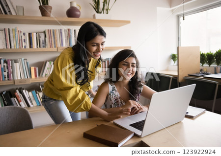 Young lady teacher mentoring female student using notebook at library 123922924