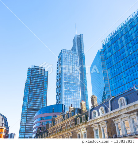 Towering skyscrapers dominate the skyline of the City of London financial district. Modern architecture contrasts with historic buildings under a clear blue sky. 123922925