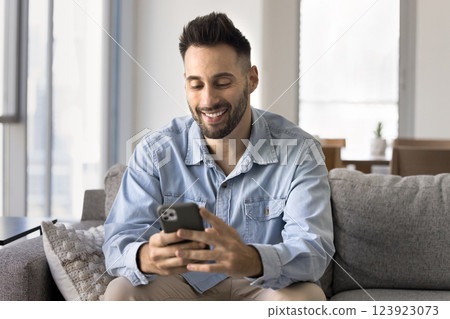 Handsome Hispanic young 30s man using smartphone seated on sofa Handsome Hispanic young 30s man using smartphone seated on sofa 123923073